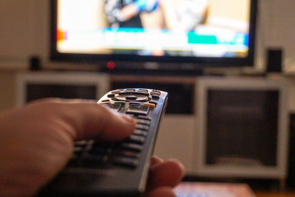 Hand holding a tv remote control while watching tv